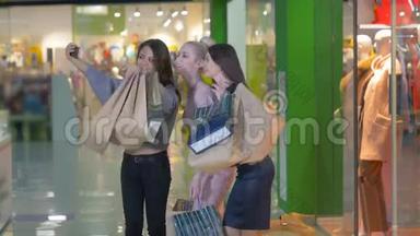 三个漂亮的年轻女孩拿着<strong>购</strong>物袋，拍照，自拍。 女孩们笑着笑着看着